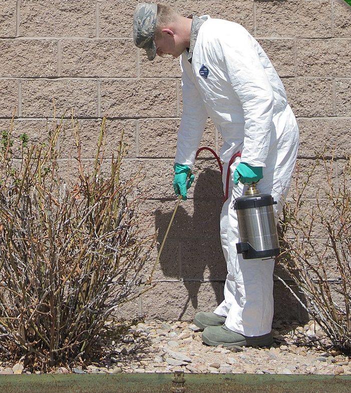 Técnico de macacão branco aplicando produto contra pragas no rodapé de um muro